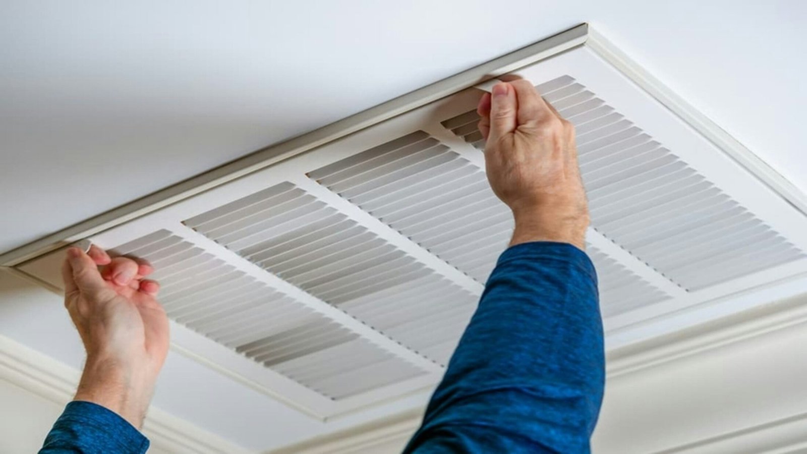 Technicien déposant la grille d’une bouche de climatisation au plafond avant son nettoyage